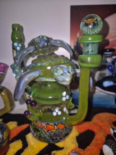 A decorative green glass water pipe with intricate designs and multiple coloured accents.