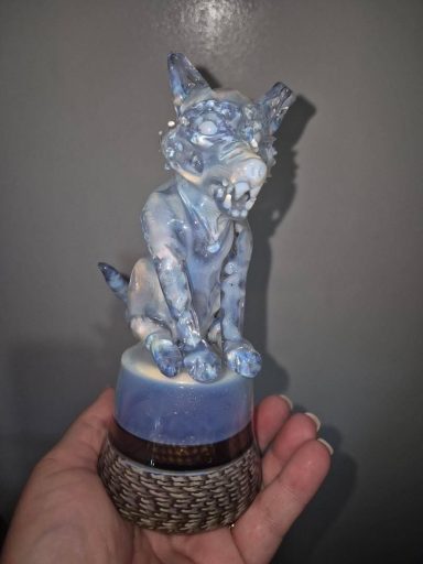 A blue and white ceramic figurine of a sitting dog on a patterned base.
