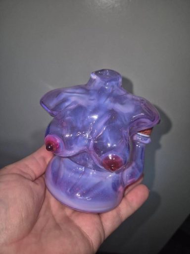 A hand holding a small, purple, glass figurine with a whimsical design.
