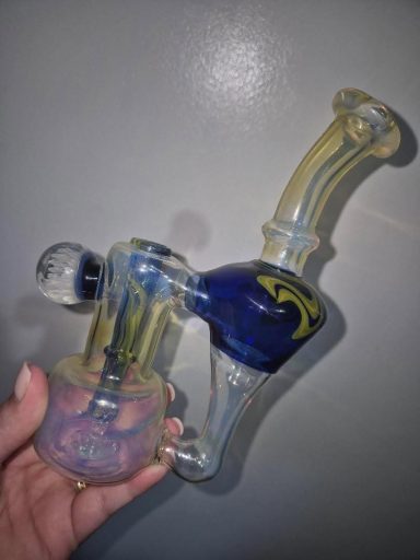 A hand holding a colourful glass water pipe with intricate designs.